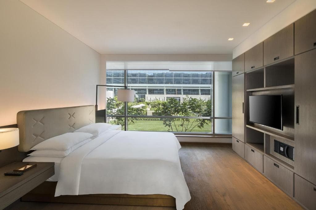 A loft-style guest room at Andaz Delhi with a king bed and a floor-to-ceiling window overlooking the property's landscaped grounds.